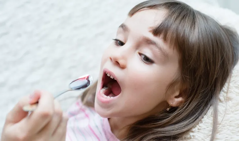 Criança de boca aberta e colher com remédio líquido sendo levada a ela