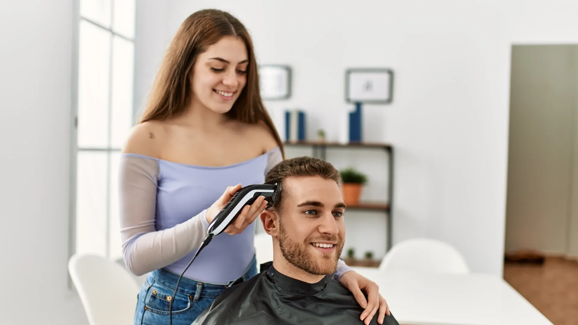 Mulher cortando o cabelo de um homem na sala de casa usando máquina de cortar cabelo