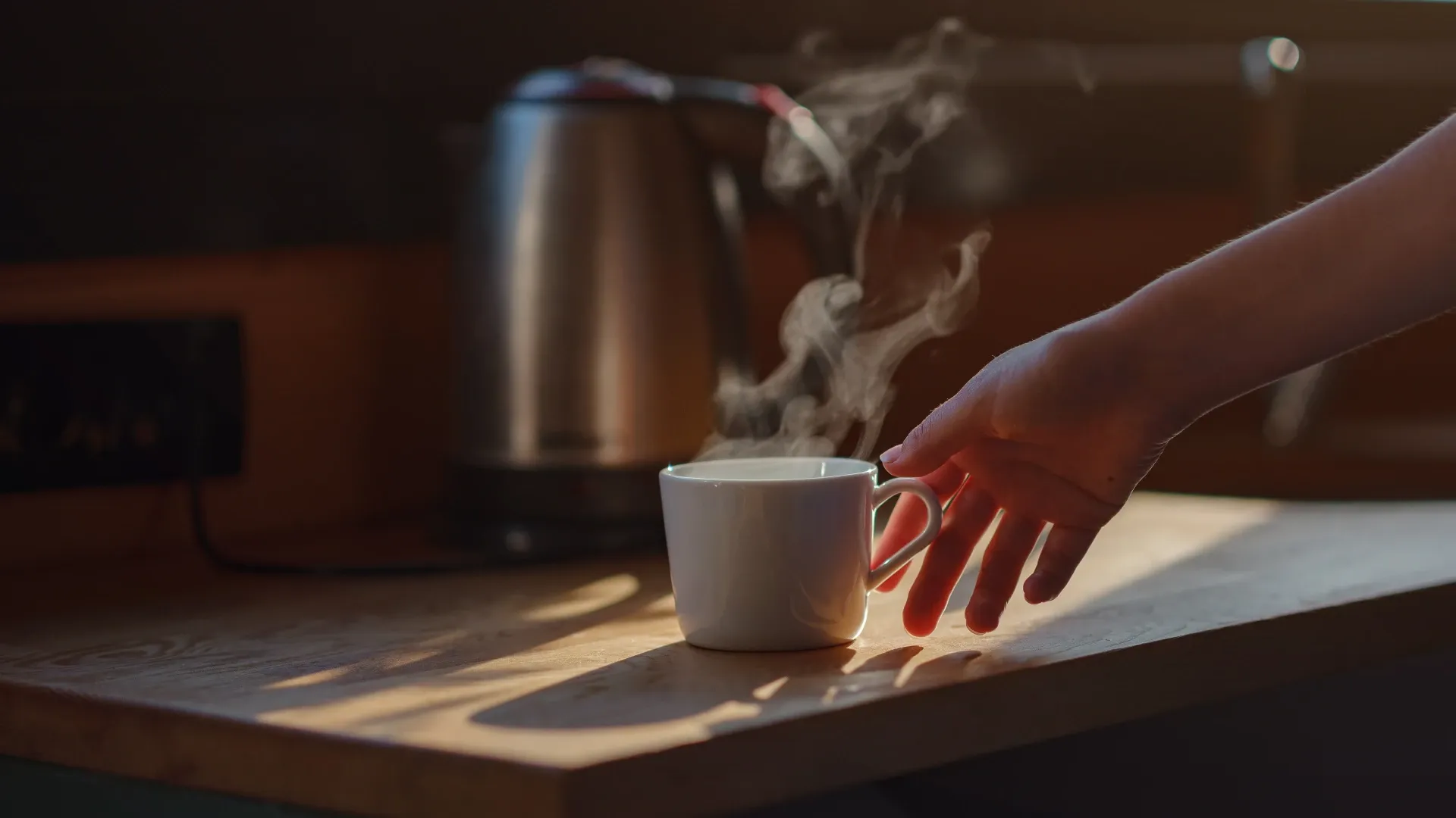 Mão quase alcançando uma xícara de café com fumaça saindo por cima