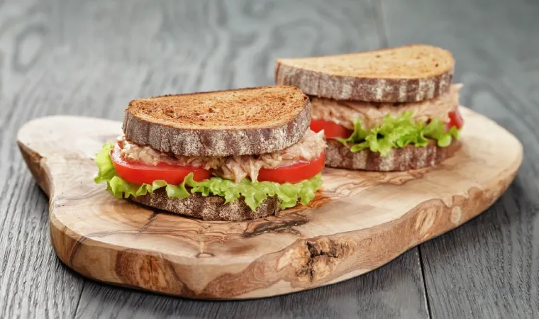 Foto de dois sanduíches naturais de frango sobre tábua de madeira.