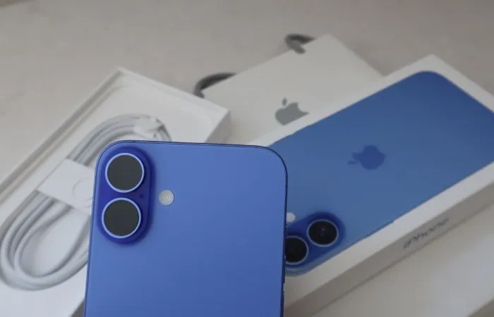 iPhone azul com caixa e carregador sobre mesa.