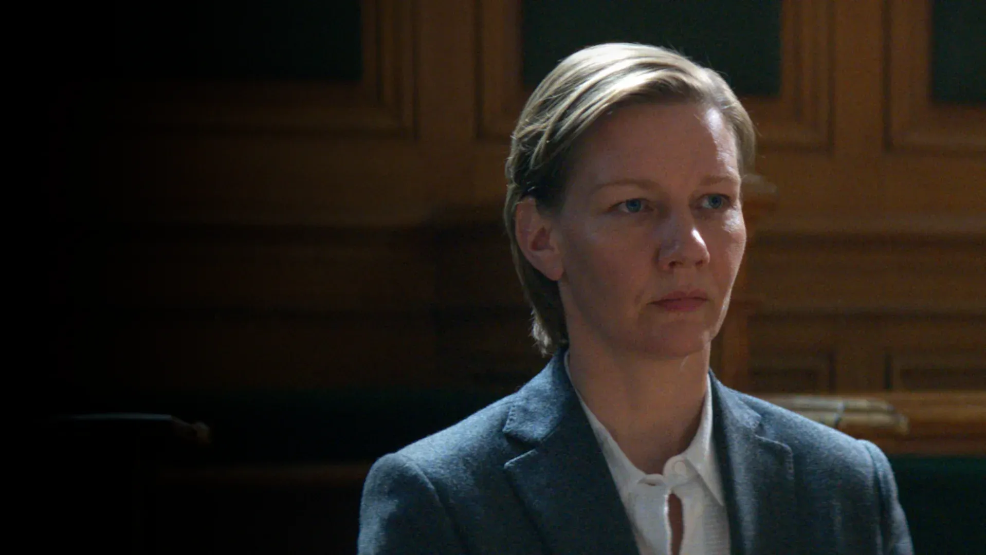 Atriz sentada em uma cadeira em um tribunal com um fundo escuro