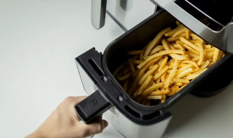 Mão abre cesto de air fryer com batata frita dentro.
