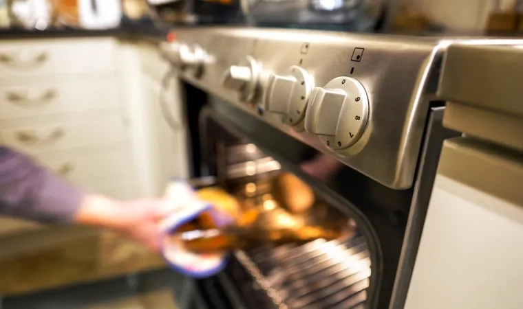 Pessoa tirando comida de dentro de forno de fogão 5 bocas a gás.