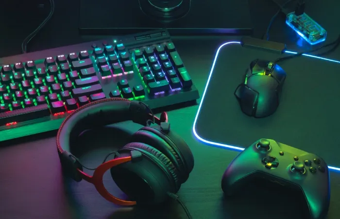 Um headset está sobre uma mesa ao lado de um setup de computador e um controle de vídeo-game