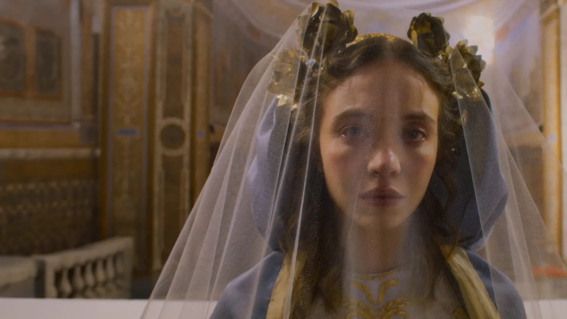 A atriz com um véu cobrindo seu rosto enquanto sua expressão é emotiva e séria em uma igreja