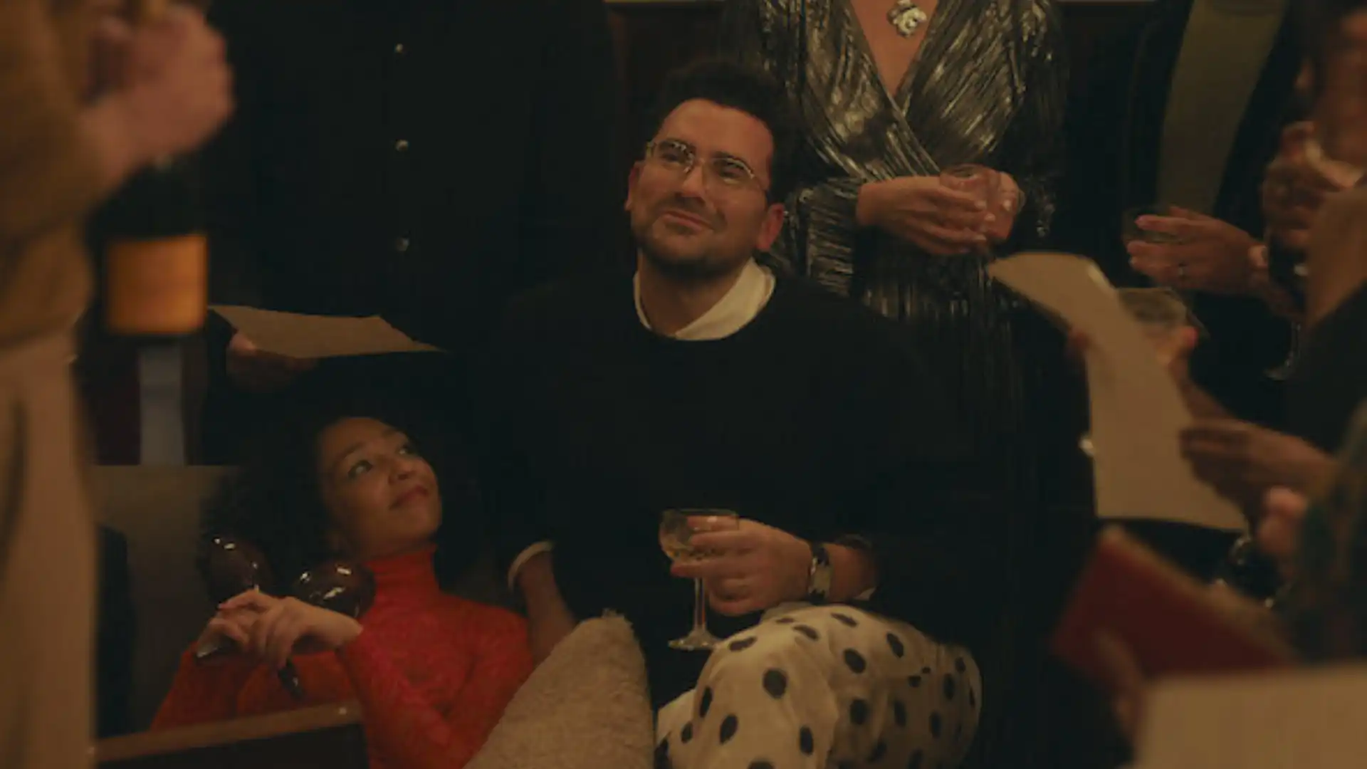 Personagem principal cercado de pessoas enquanto admira alguém sorrindo