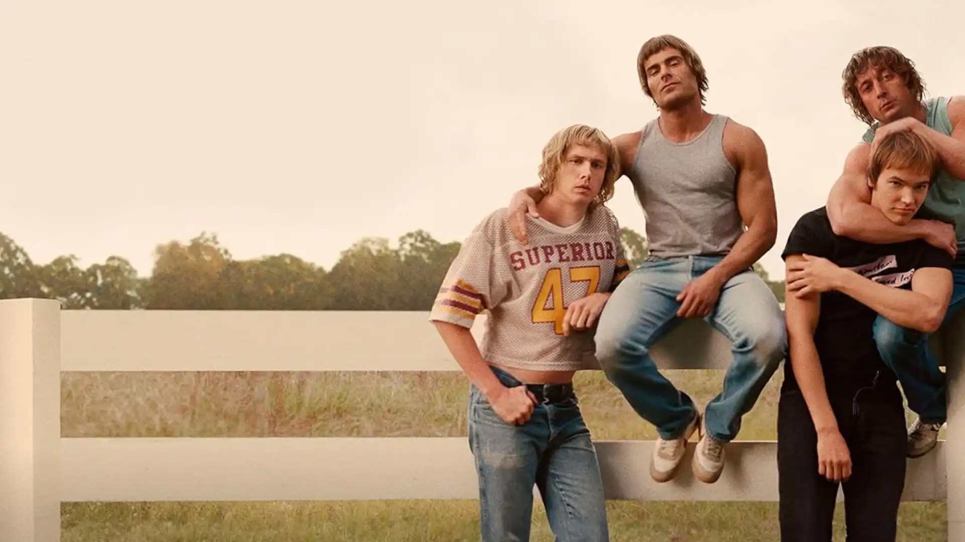 Quatro homens sentados em um cercado branco com uma fazenda no fundo