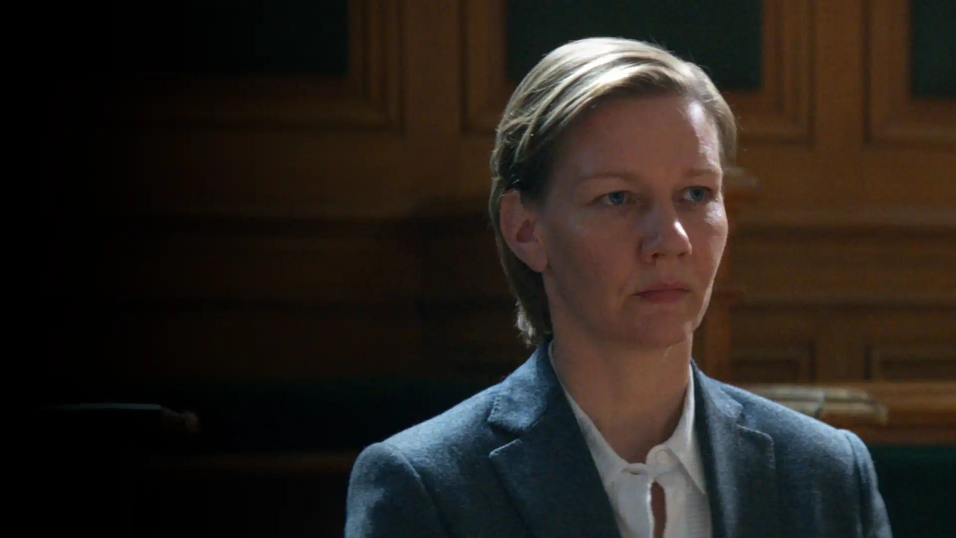 Personagem principal sentada em um tribunal enquanto é julgada com fundo escuro