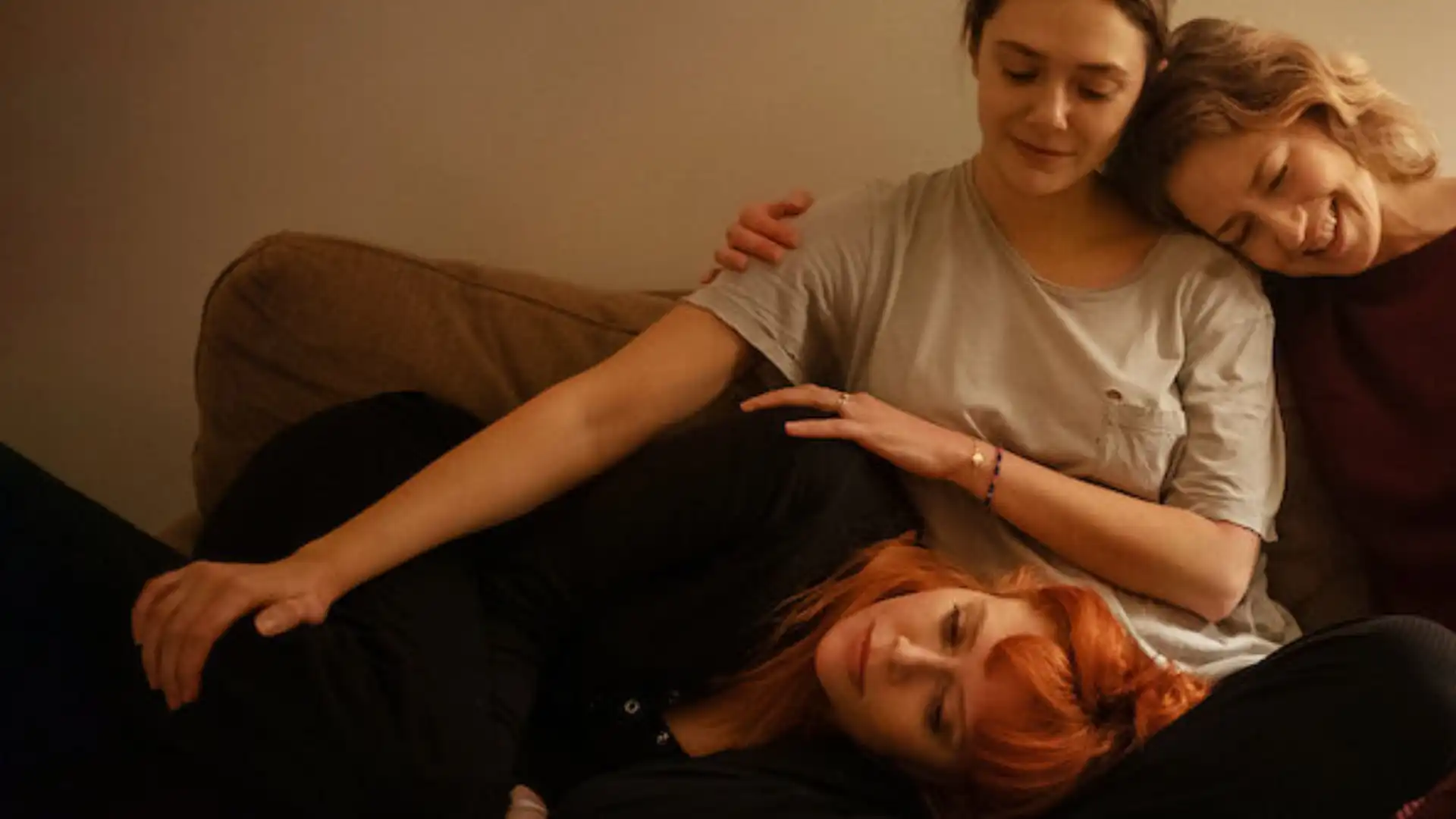 Três mulheres abraçadas no sofá enquanto sorriem