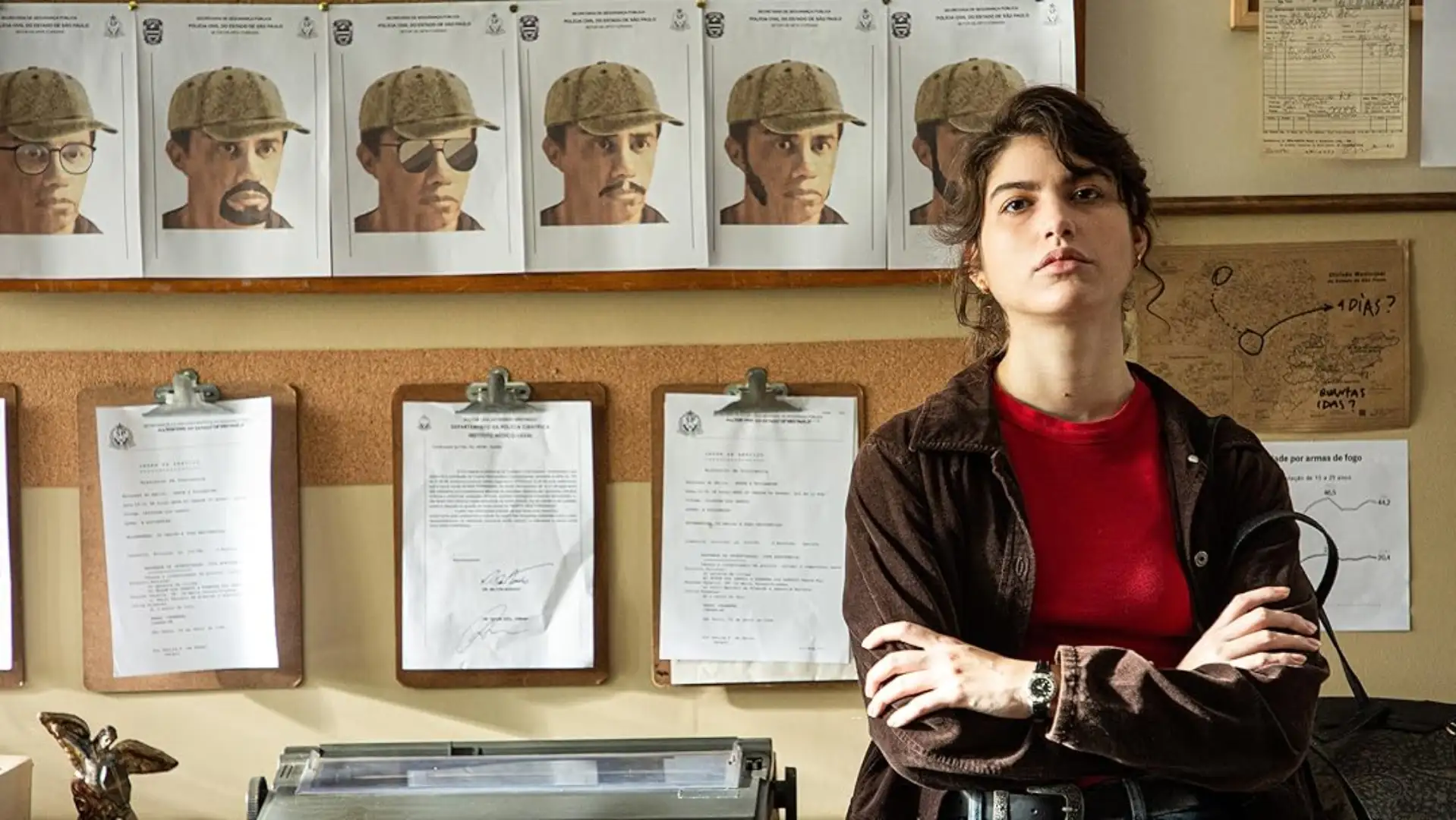 Atriz encarando com uma expressão séria com retratos falados diversos no fundo