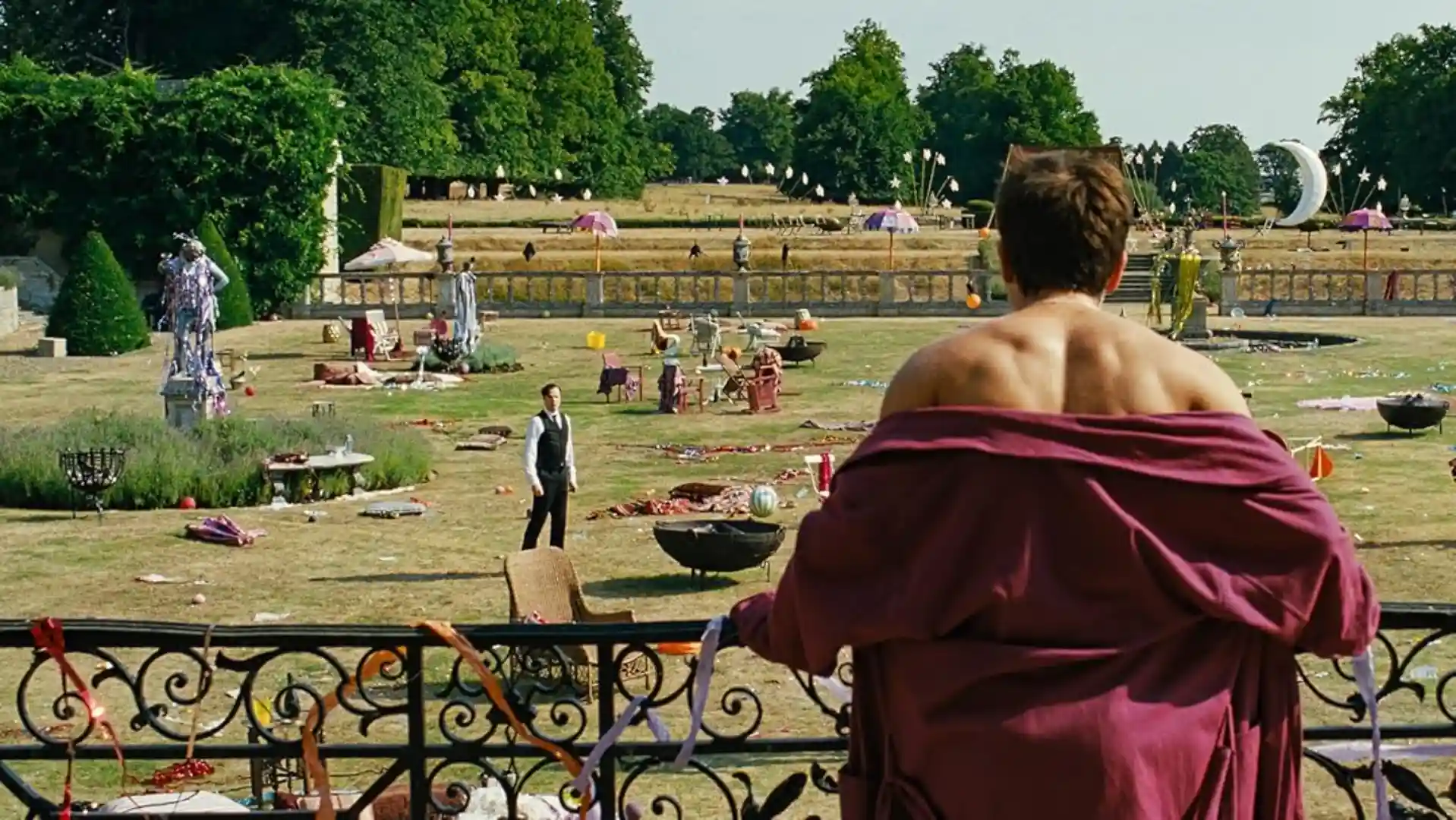 Homem de roupão com costas aparecendo enquanto olha para um homem no jardim que está repleto de coisas espalhados no quintal