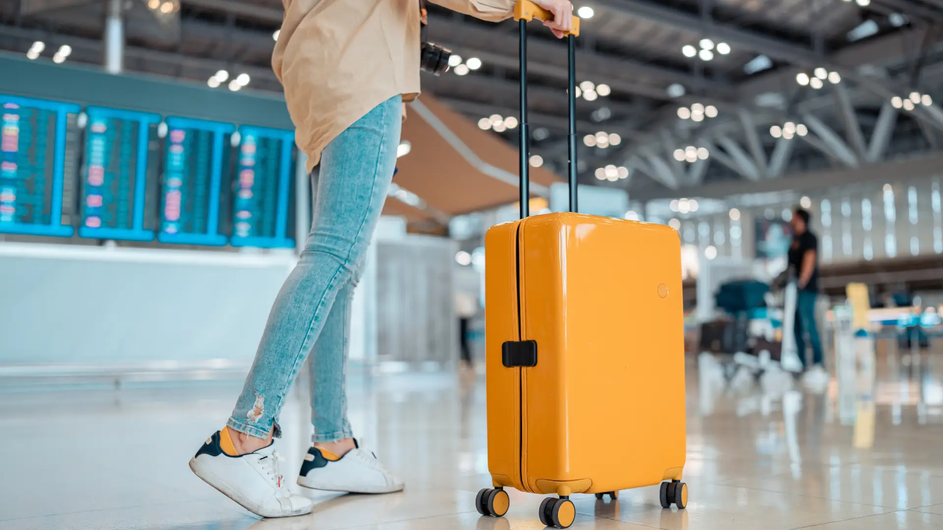 Pessoa levando mala de viagem amarela com rodinhas em um aeroporto.
