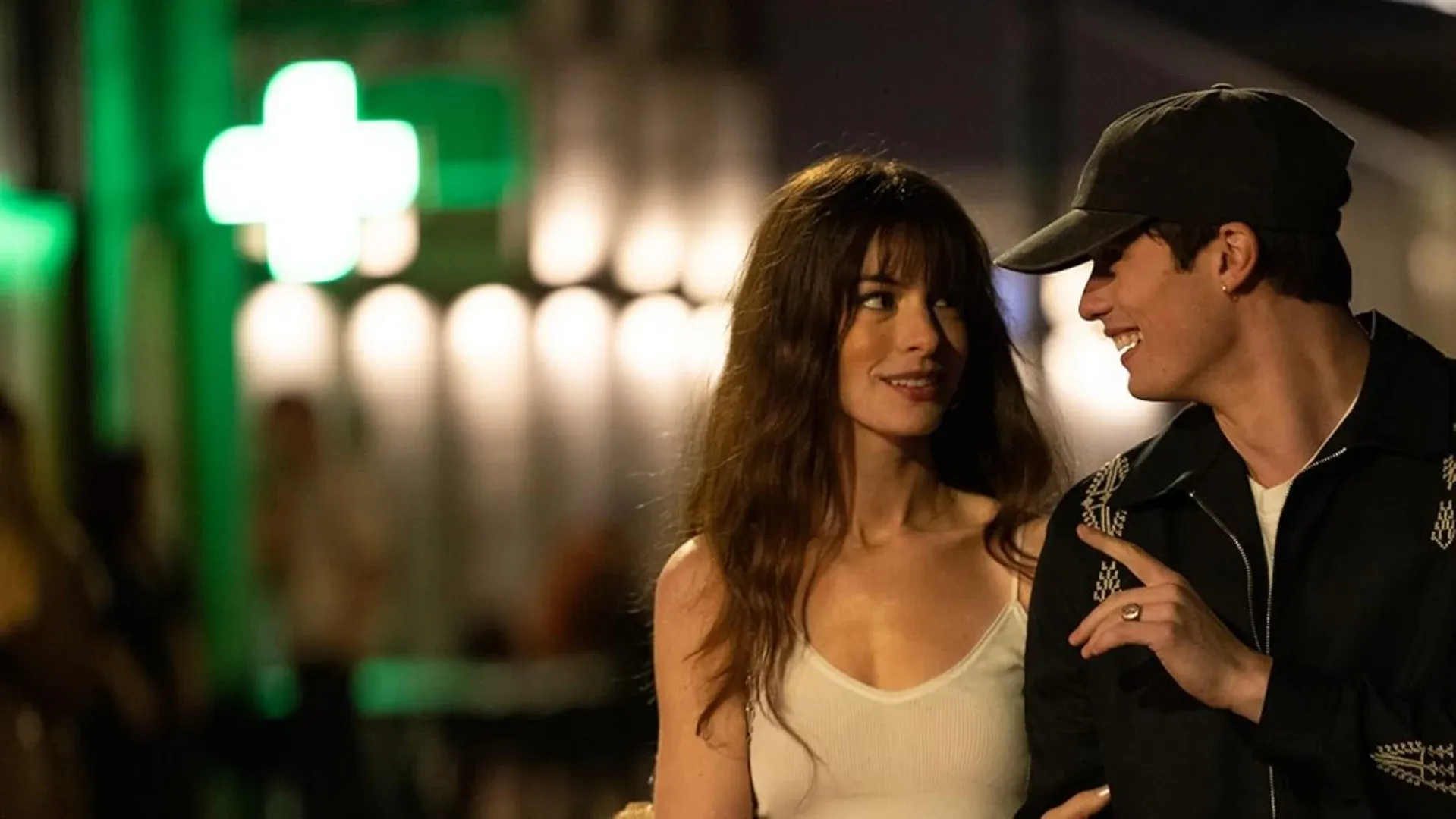 Atores se olhando enquanto sorriem e caminham por uma rua iluminada