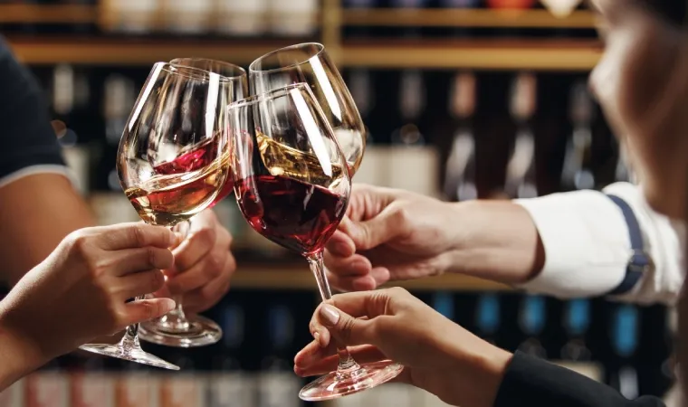 Grupo brinda segurando taças de vinho branco e tinto
