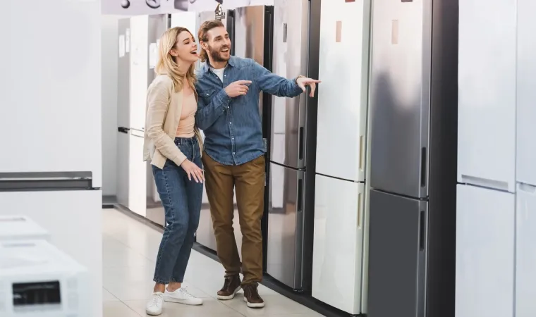 Casal de homem e mulher jovens analisa modelos de geladeira em loja de eletrodomésticos.
