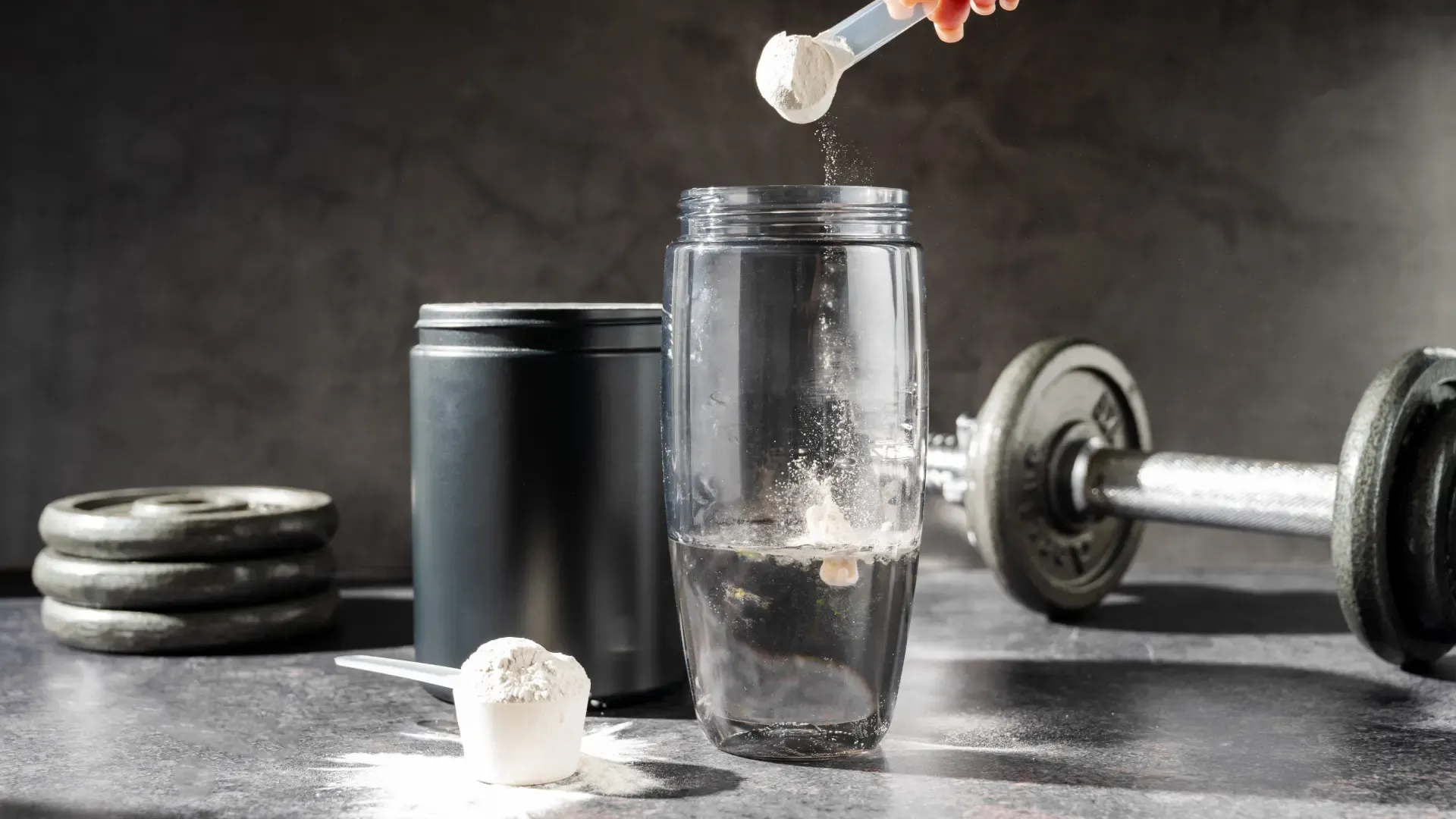 Creatina monohidratada em pó sendo despejada em um shaker, ao lado de equipamentos de academia