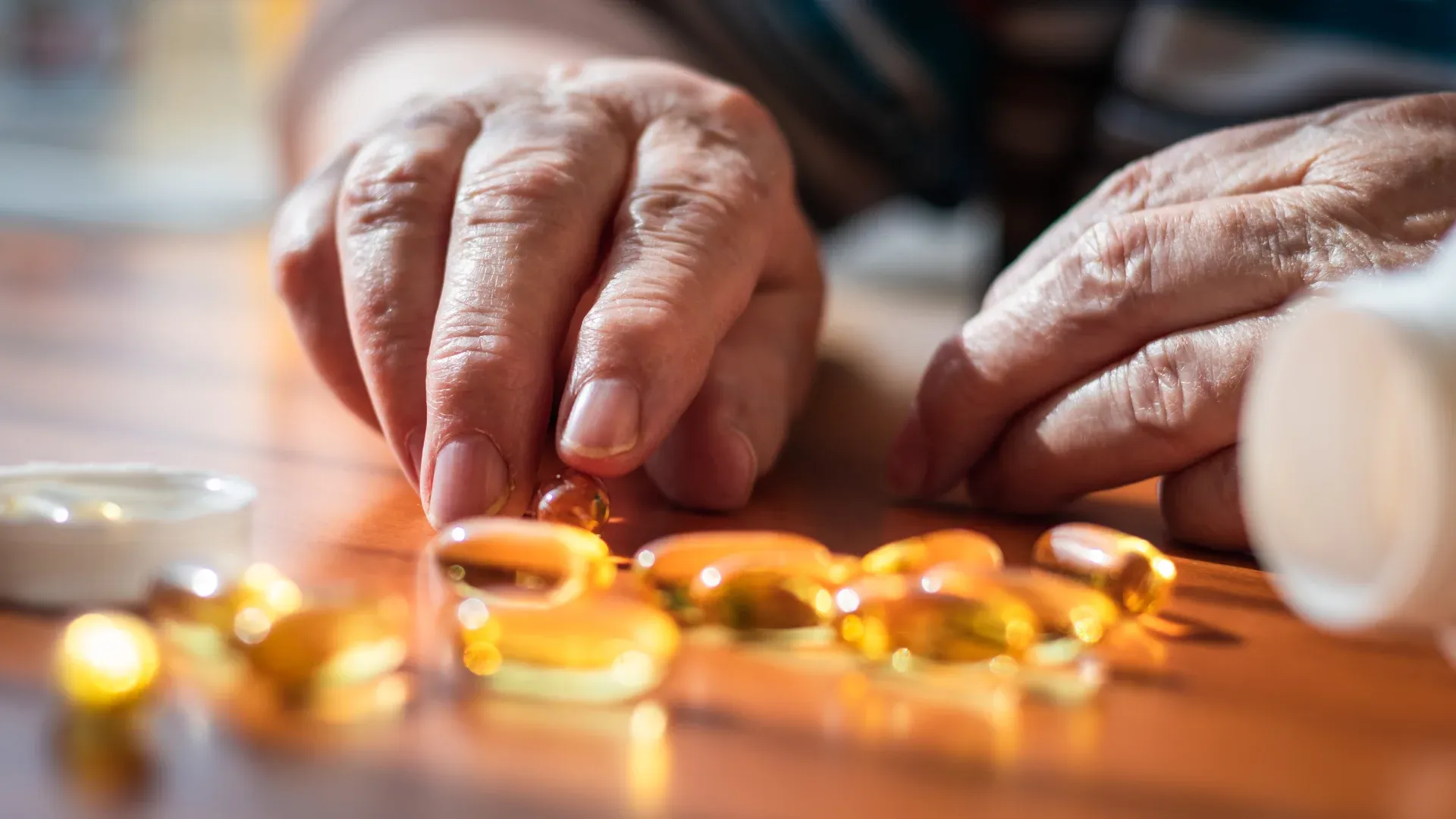  Mãos femininas idosas pegando uma cápsula de suplemento na mesa