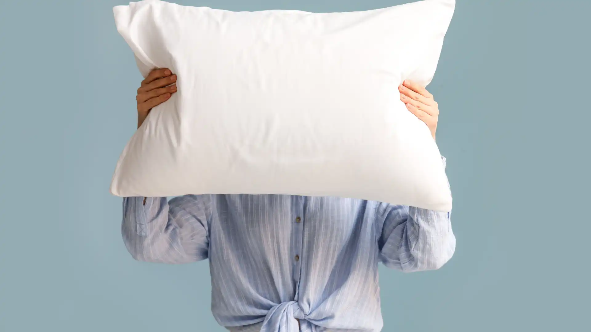 Uma mulher está segurando um travesseiro branco em frente ao rosto.