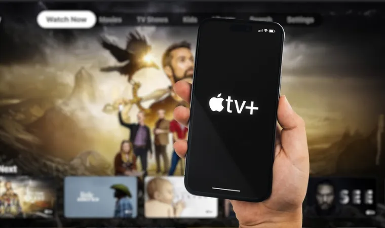 Imagem de uma pessoa segurando um iPhone com o símbolo da Apple TV+ na frente de uma TV com o app da Apple TV
