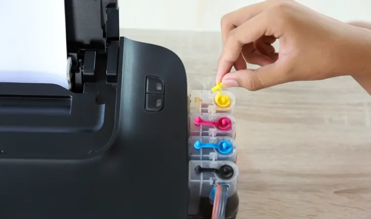 Uma impressora vista de cima enquanto alguém mexe nos tanques de tinta.