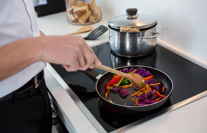 Homem preparando legumes em um cooktop de indução.