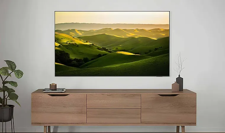 TV DU 7700 na parede exibe colinas verdes ao pôr do sol acima de estante moderna.