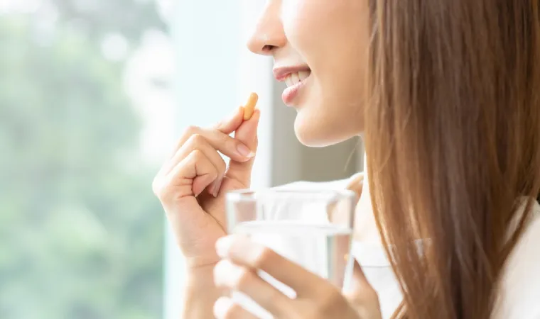 Mulher sorrindo segurando um copo de água com uma cápsula na mão 