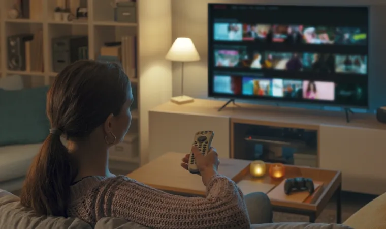 Mulher vendo TV enquanto mexe no controle remoto