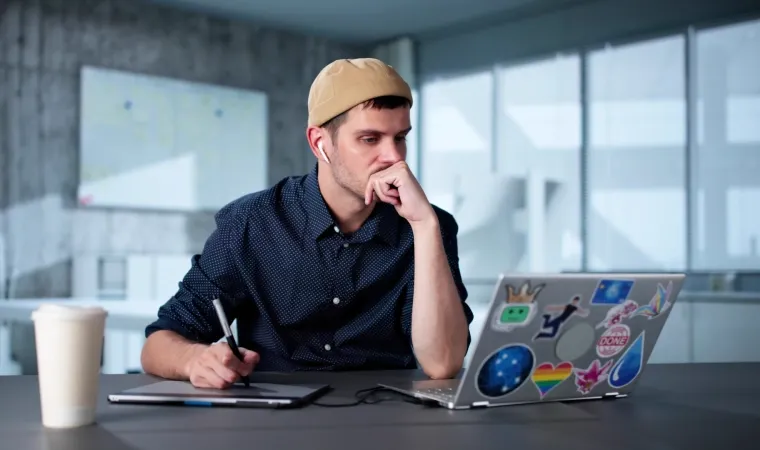 Homem de touca em escritório usando o seu notebook para designer gráfico