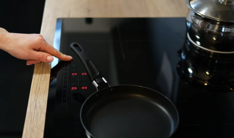  Mão feminina ligando cooktop com frigideira inox sobre uma das bocas