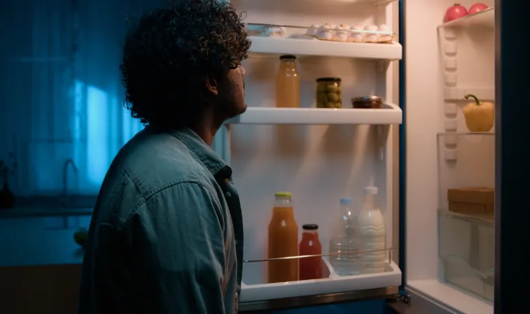 Homem com porta de geladeira aberta confere interior do aparelho