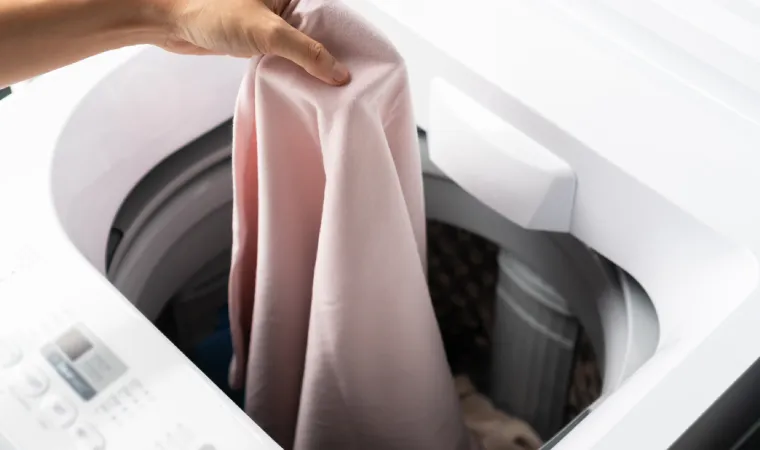 mão feminina colocando roupa dentro de máquina de lavar com abertura superior