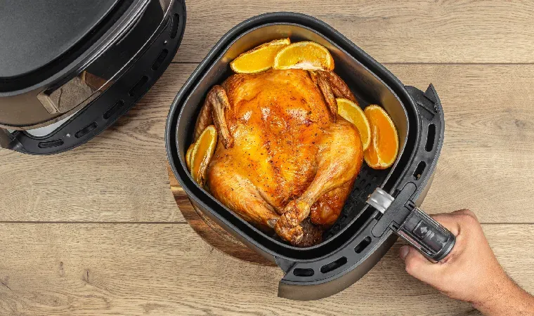Visão de cima mostra cesto de air fryer com frango inteiro assado com laranjas.
