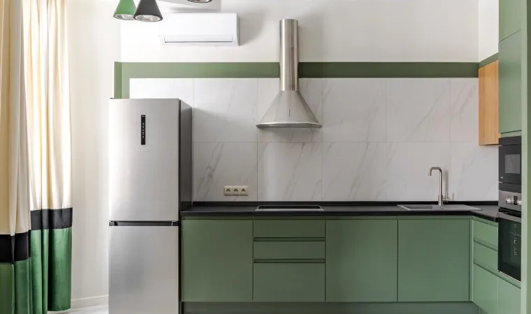 Geladeira inox posicionada ao lado de bancada verde em cozinha moderna 