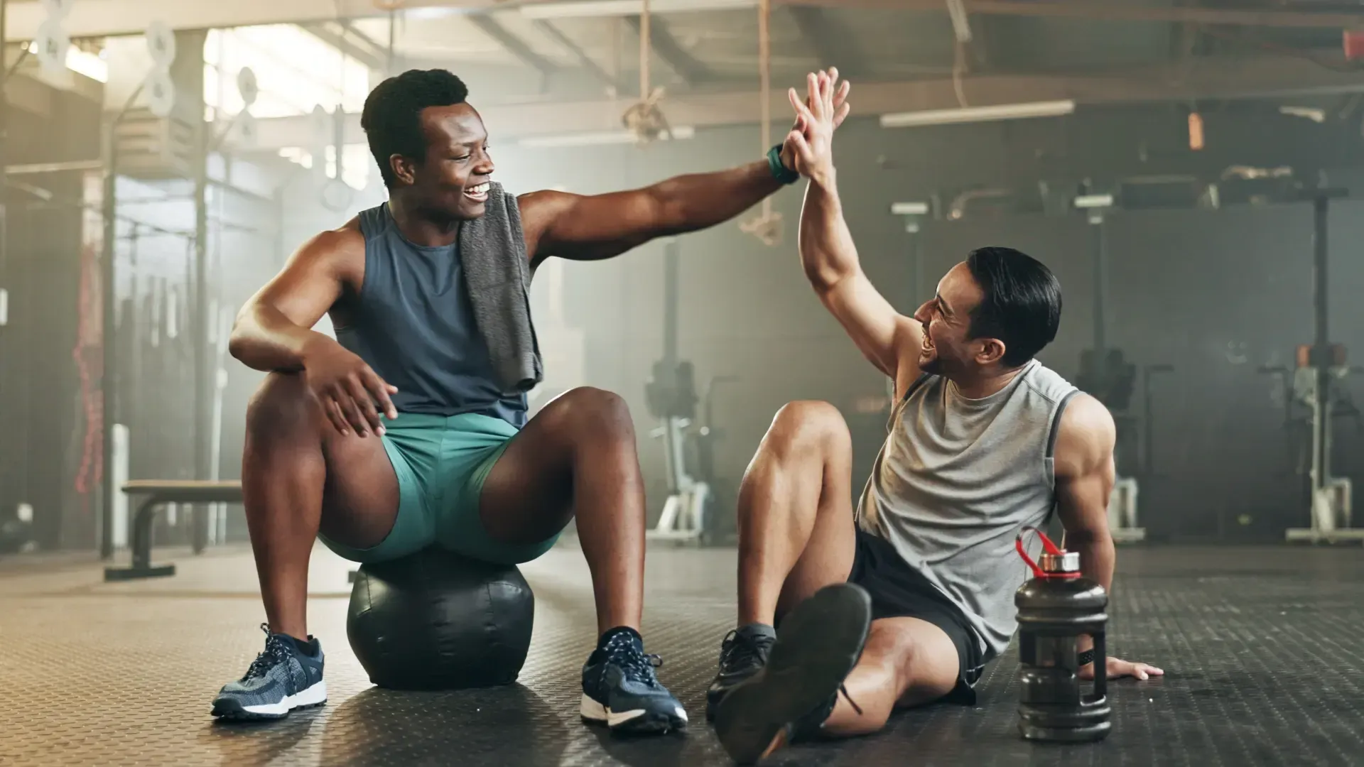 Imagem de duas pessoas na academia se cumprimentando enquanto fazem um exercício físico