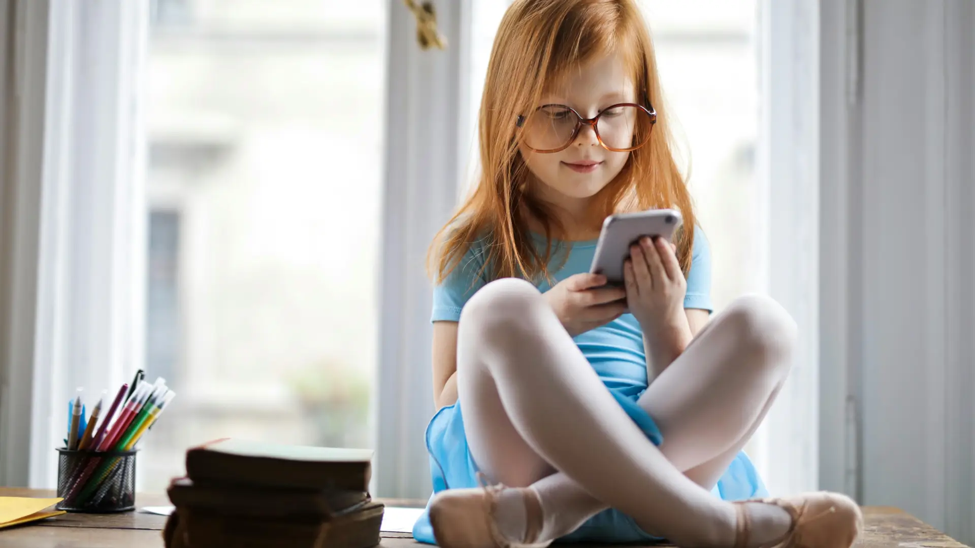 Uma menina está sentada em uma mesa comum celular em mãos