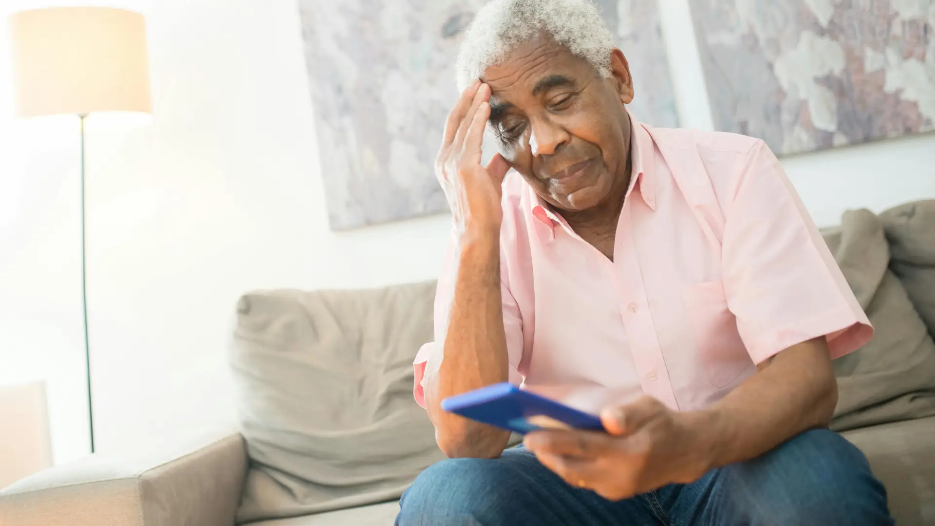 Senhor sentado em sofá com a mão na cabeça usando o seu celular para idosos 