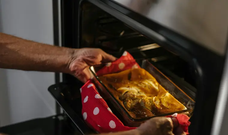 Imagem de uma travessa de comida sendo tirada do forno elétrico 