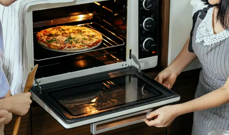 Imagem de duas pessoas prestes a tirar uma pizza de um forno elétrico