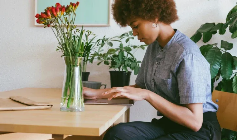 Mulher sentada em cadeira usando o seu tablet bom e barato ao lado de flores