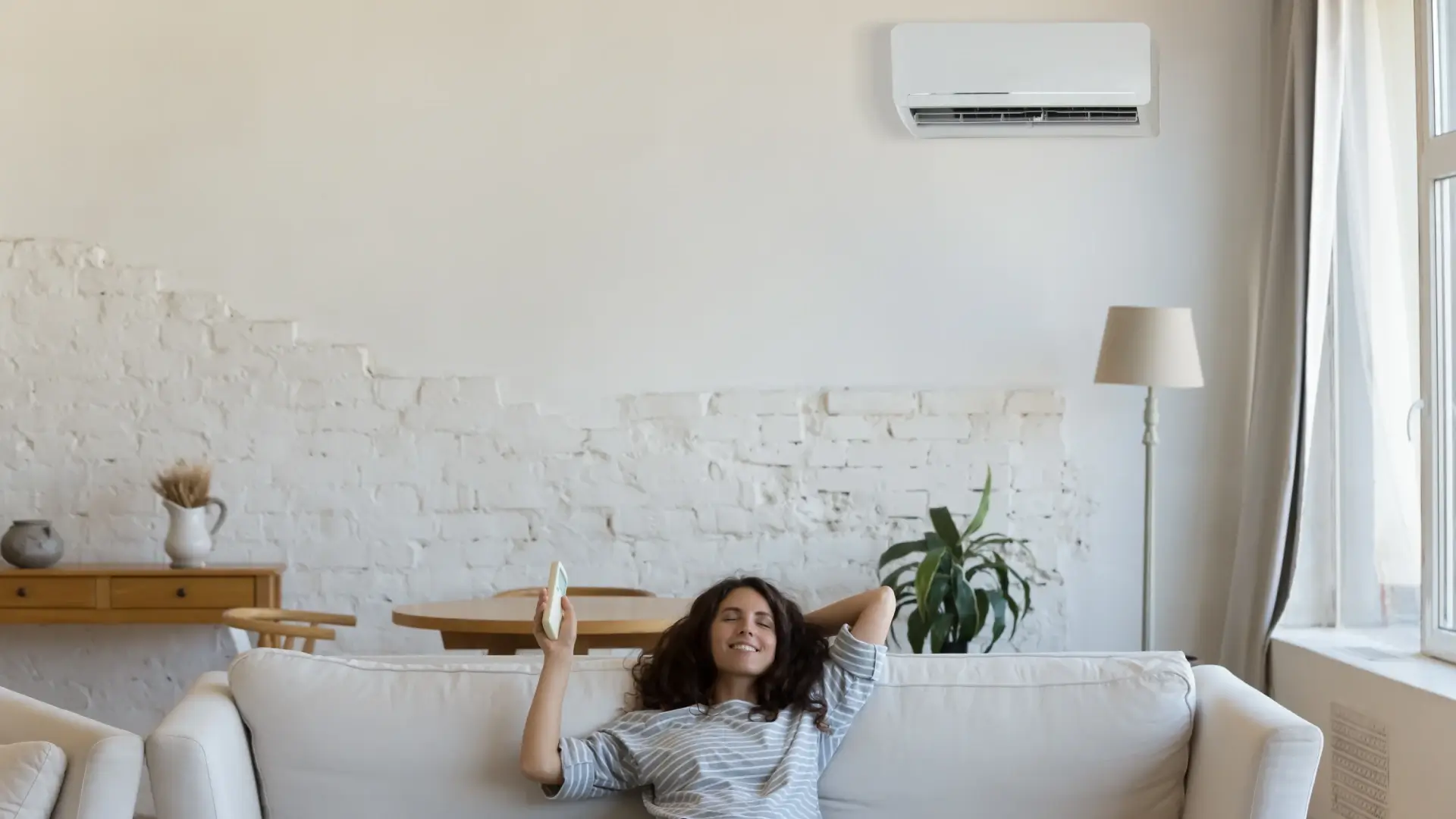 Jovem mulher sentada no sofá aproveitando o ar-condicionado Inverter 9.000 BTUs