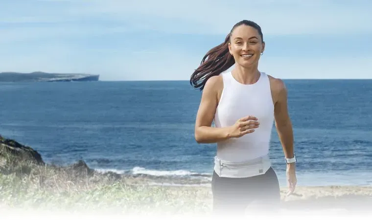 Uma mulher com roupa de academia está correndo e sorrindo enquanto olha para frente 