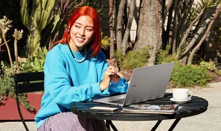 Mulher ruiva trabalha com um notebook Samsung Galaxy Book3 360 em uma mesa em área externa durante dia ensolarado