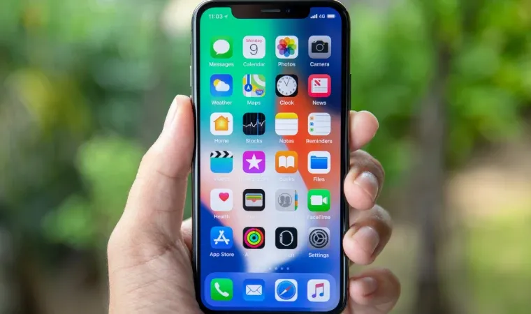 iPhone XS nas mãos de homem com folhas verdes ao fundo 