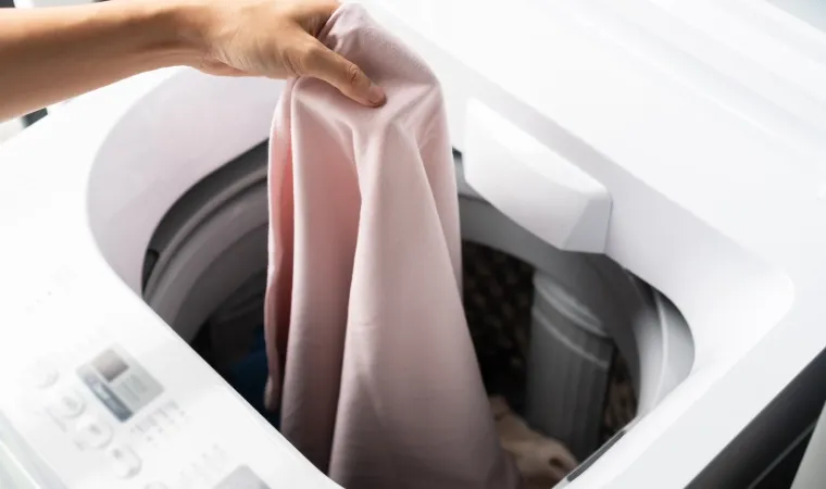 Mão feminina colocando roupa dentro da máquina de lavar Brastemp.