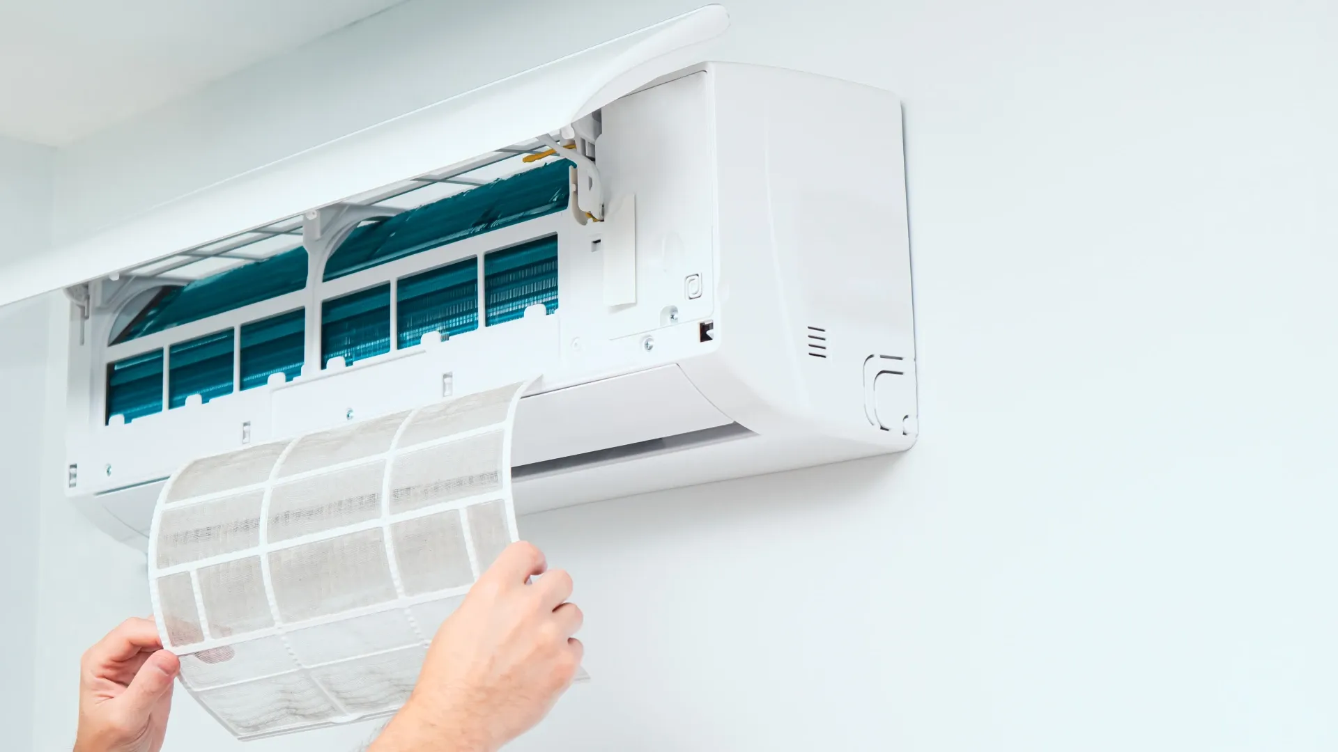 Imagem de duas mãos retirando o filtro de um ar-condicionado 