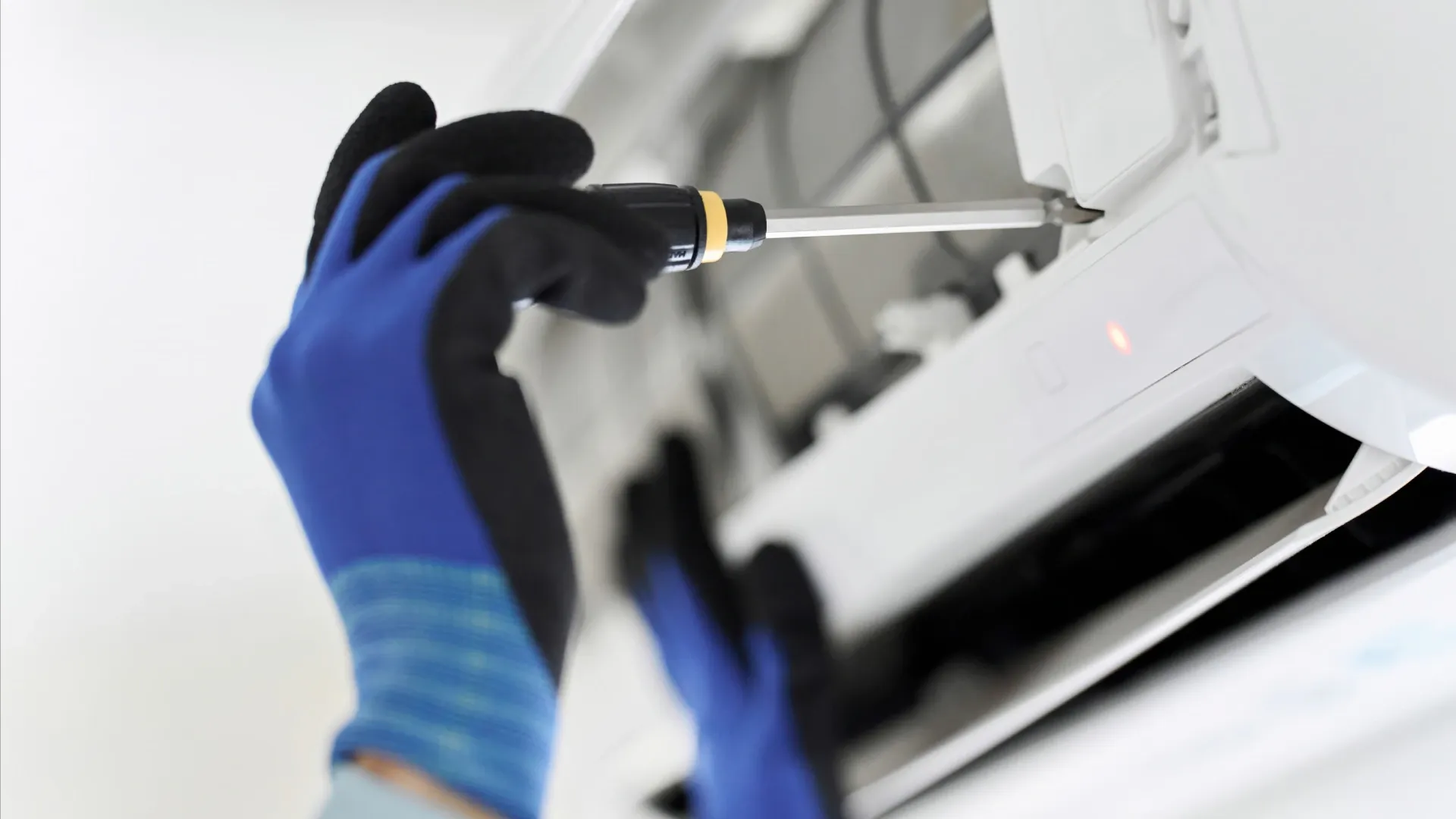 Imagem de uma mão com uma chave desparafusando uma peça de um ar-condicionado 