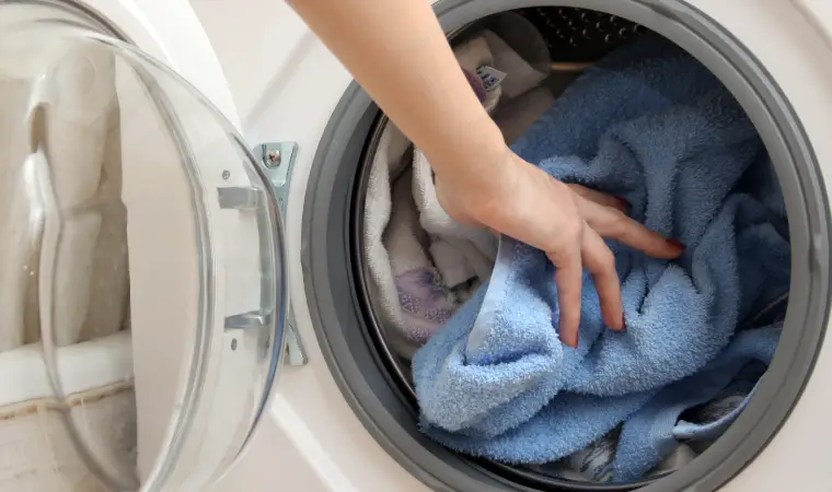 Imagem de uma pessoa colocando roupas para lavar na máquina