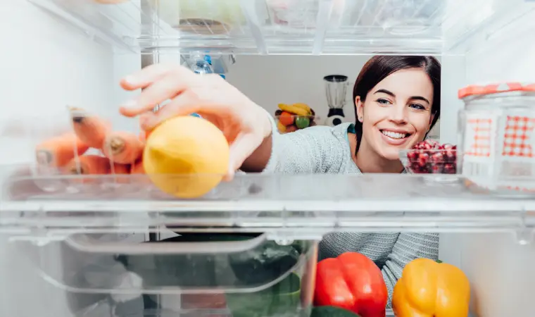 Mulher pegando uma fruta da geladeira Midea